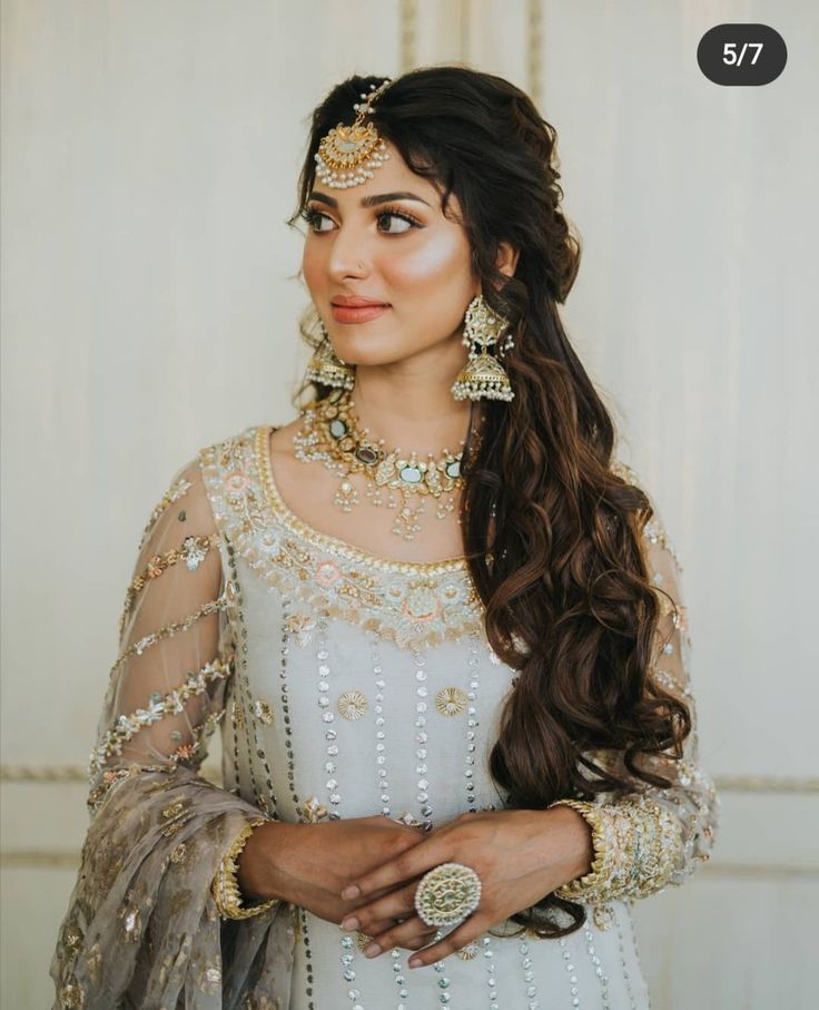 a woman with long hair wearing a white dress and gold jewelry is posing for the camera