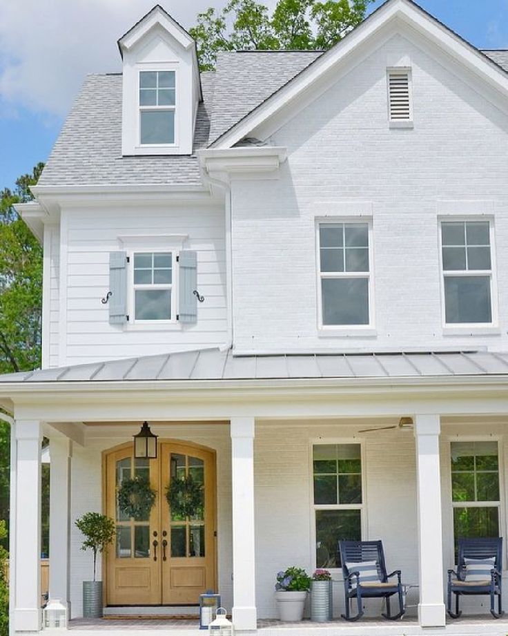 a large white house with two chairs on the front porch and one chair sitting outside