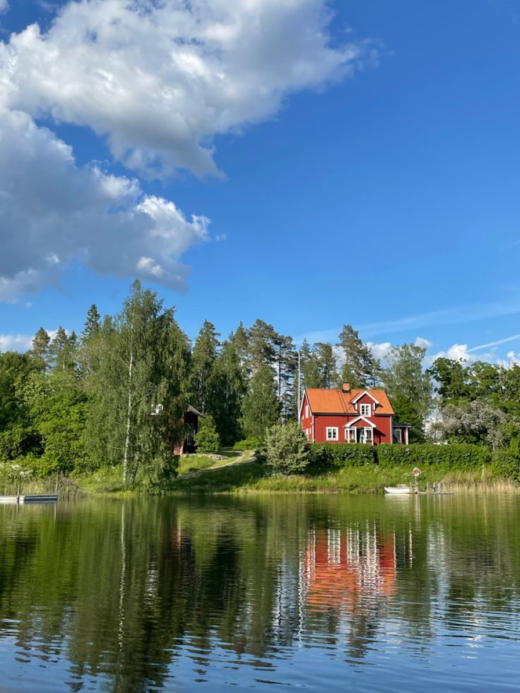 a red house sitting on top of a lush green hillside next to a lake and forest