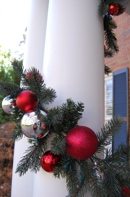 a white pillar decorated with red and silver ornaments, pine branches and christmas balls hanging from it