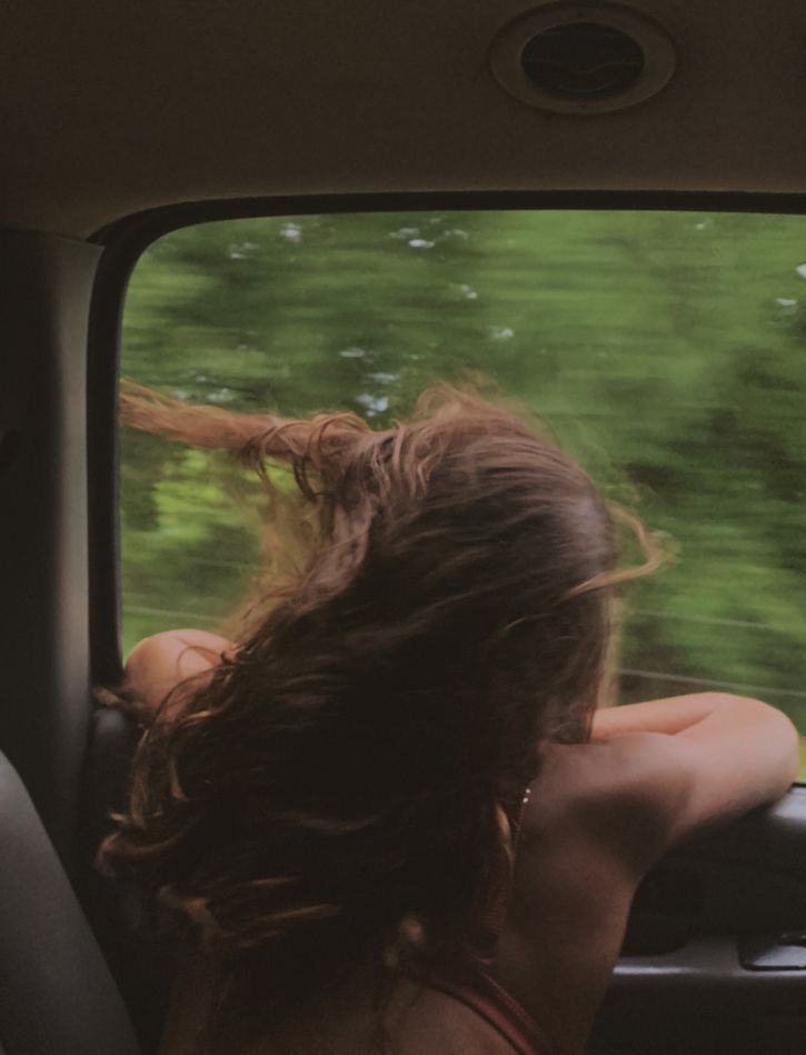 a woman sitting in the passenger seat of a car looking out the window at trees