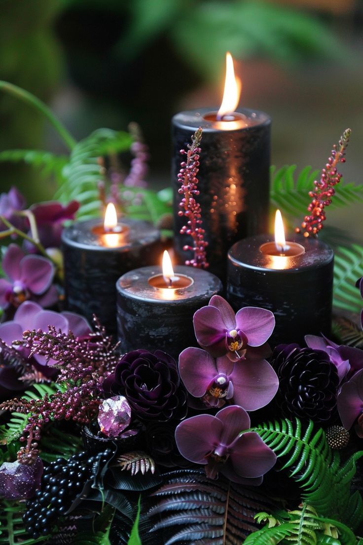 three lit candles surrounded by purple flowers and ferns