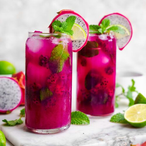 two glasses filled with pink lemonade, lime and mint garnish on a marble tray