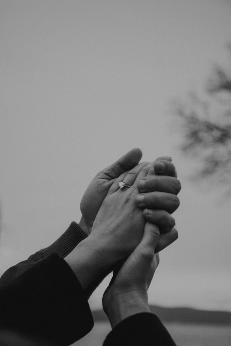 two people holding hands in front of a tree with the sky in the back ground