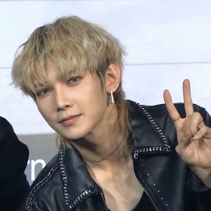 a man with blonde hair wearing a black leather jacket and peace sign in front of him