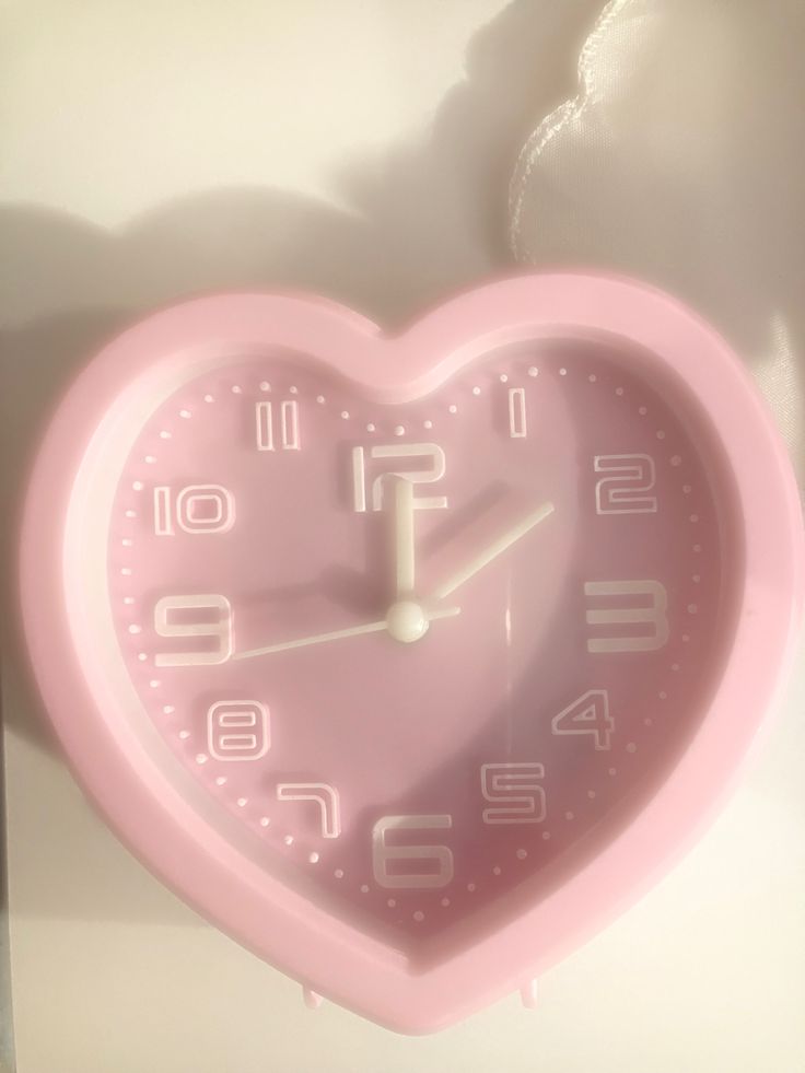 a pink heart shaped clock hanging on the wall