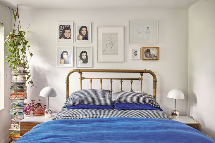 a bed with blue sheets and pictures on the wall above it, along with plants