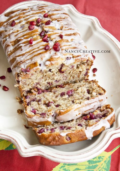 a loaf of cranberry orange bread on a white plate with icing and pomegranates