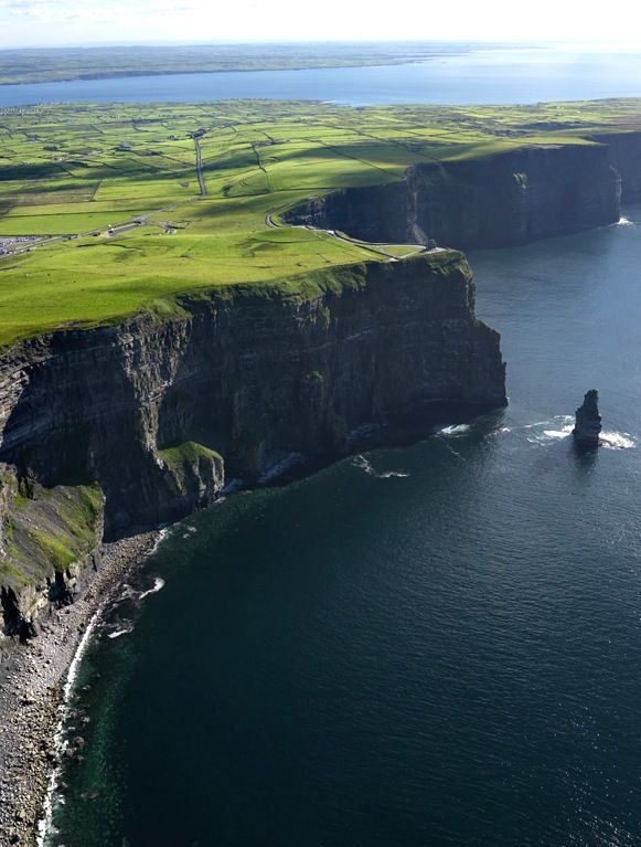 an aerial view of the ocean with cliffs and green grass on both sides, along with some water in the foreground