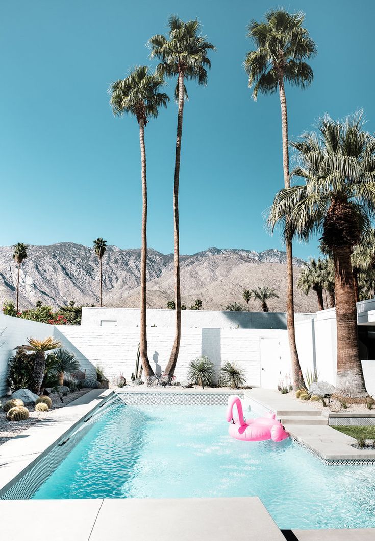 an inflatable pink flamingo sits next to a pool surrounded by palm trees