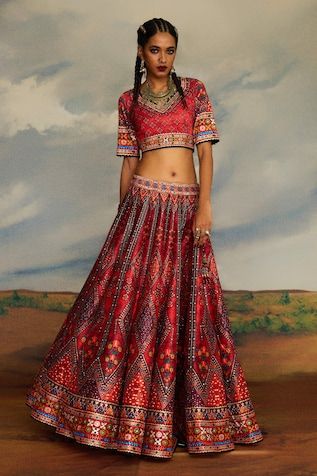 Red lehenga set featuring a V-neck blouse with tribal print and bead embroidery. Paired with a coordinating dupatta and lehenga, both showcasing intricate designs., Fit: Relaxed Festive Bohemian V-neck Choli, Red V-neck Navratri Sets, Red V-neck Choli For Navratri, Traditional Red V-neck Choli, Bohemian Style V-neck Festive Choli, Bohemian V-neck Festive Choli, Red Mirror Work Choli For Traditional Ceremonies, Bohemian Embroidered Red Lehenga, Bohemian V-neck Choli For Festivals