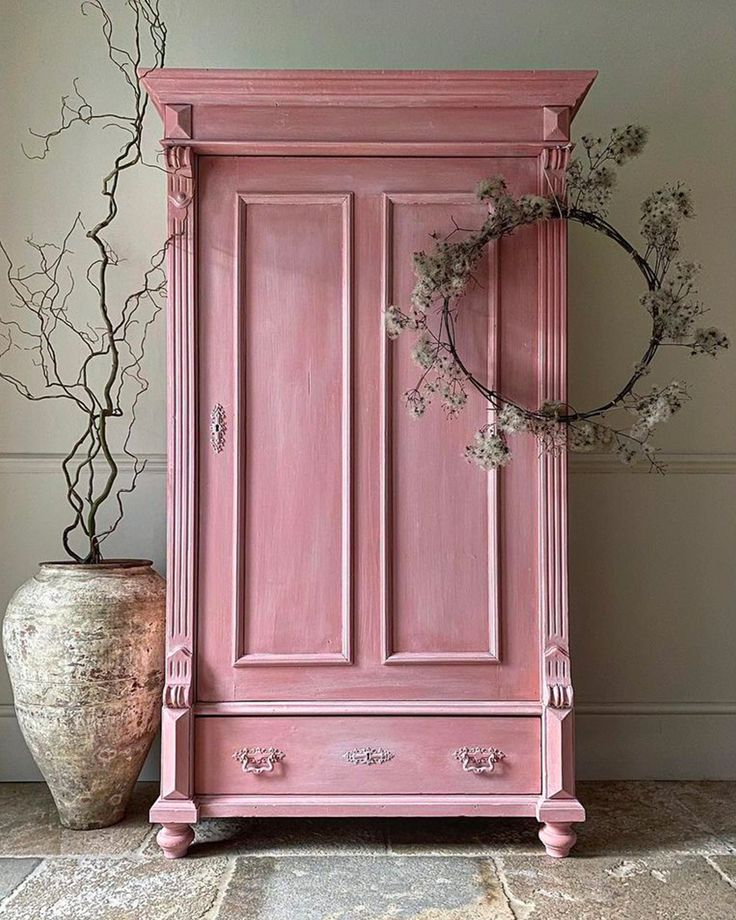 a pink armoire next to a potted plant