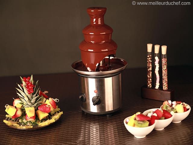 the chocolate fountain is next to three bowls of fruit and two plates of strawberries