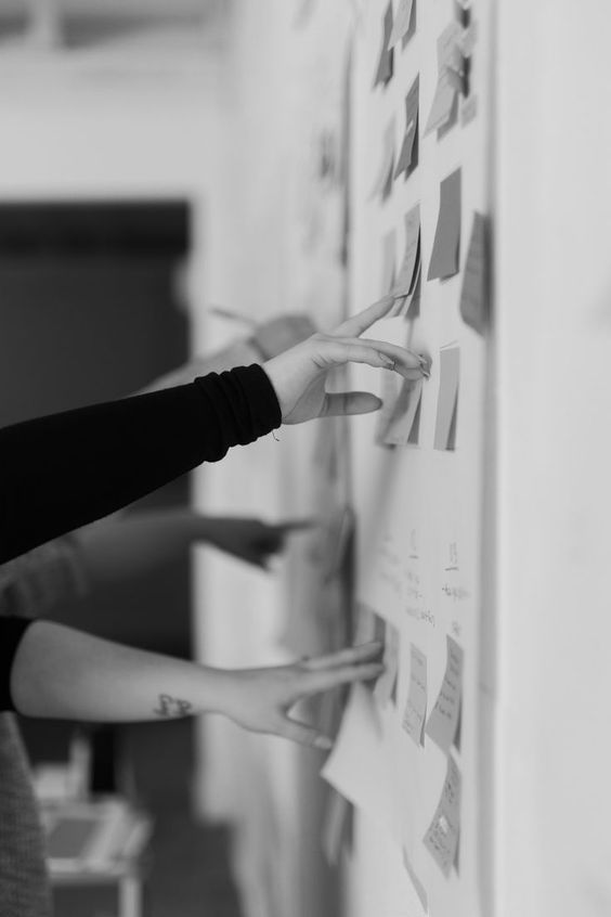 two women are writing on a wall with post it notes attached to the wall and holding their hands in front of them