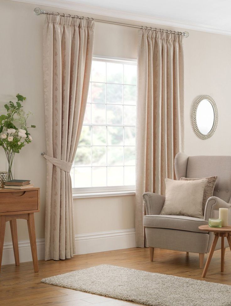 a living room filled with furniture and a large window covered in beige drapes next to a wooden table