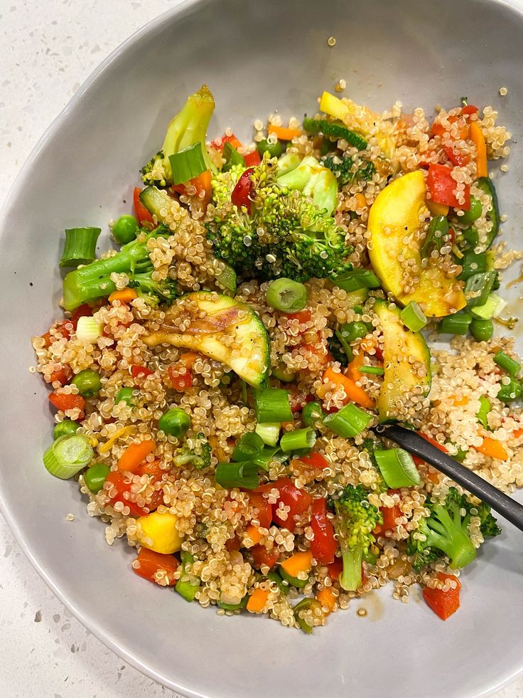 a white bowl filled with rice and vegetables on top of a table next to a fork