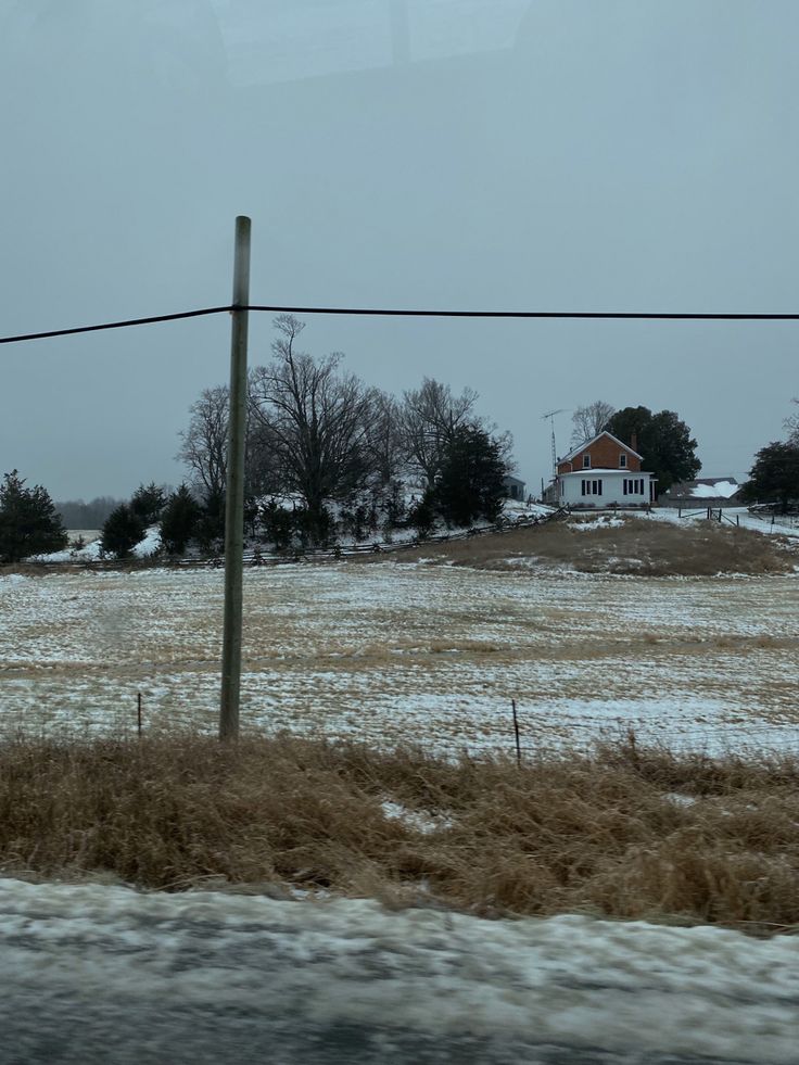 an empty field with snow on the ground and a house in the distance behind it