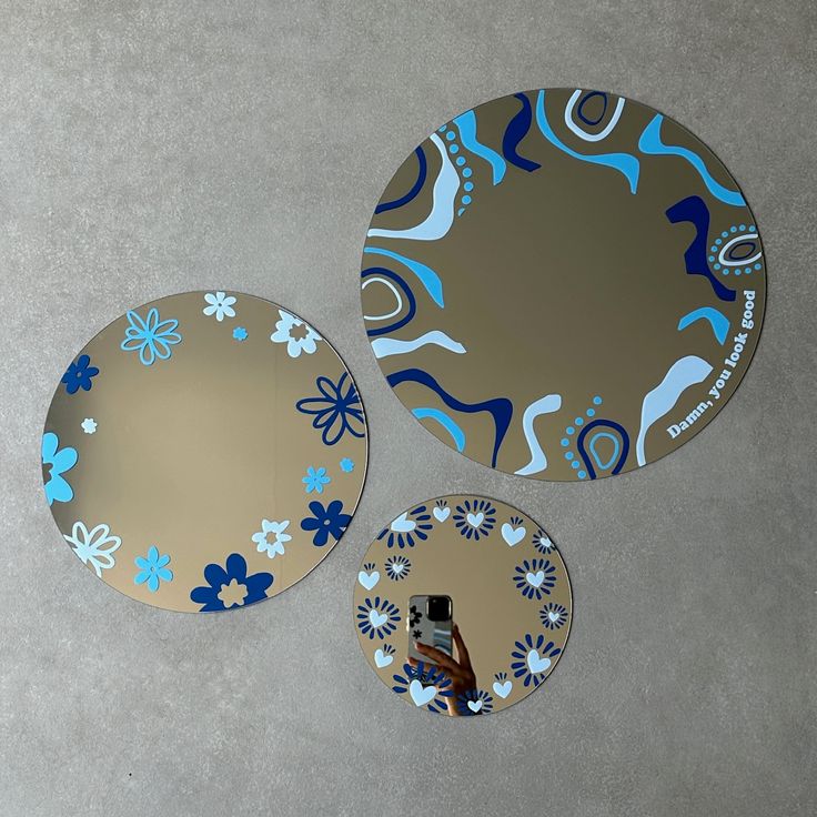 three circular mirrors with blue and white designs on them, one is holding a cell phone