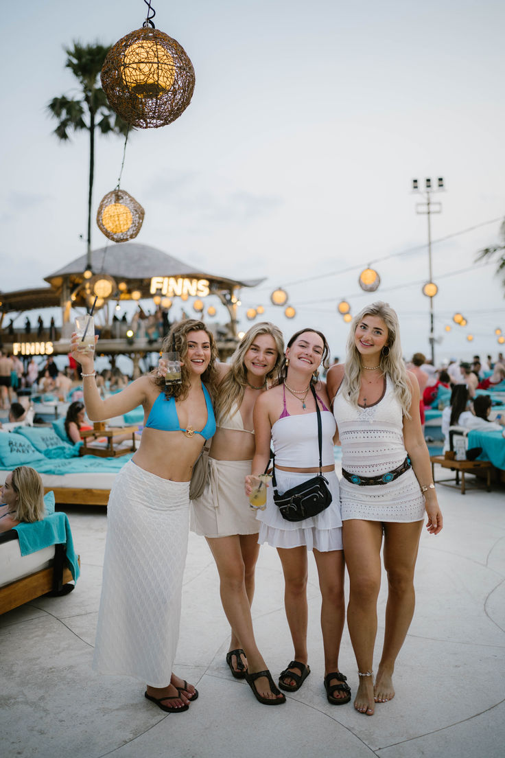 three women standing next to each other in front of a pool at night with lights hanging from the ceiling