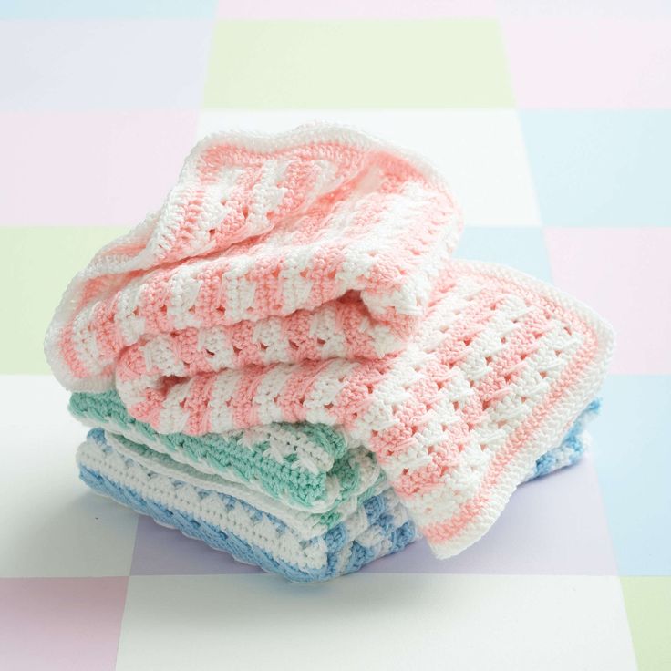 three crocheted blankets stacked on top of each other in front of a checkered tablecloth