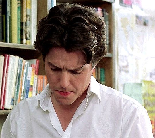 a man looking down at his cell phone in front of a bookshelf full of books