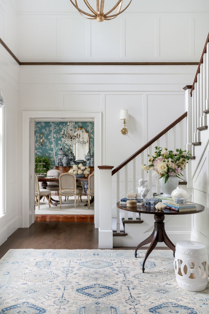 a room with a table, chair and rug on the floor in front of a staircase