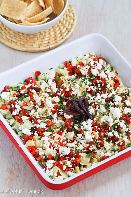 a red and white dish filled with food sitting on top of a table next to a pizza