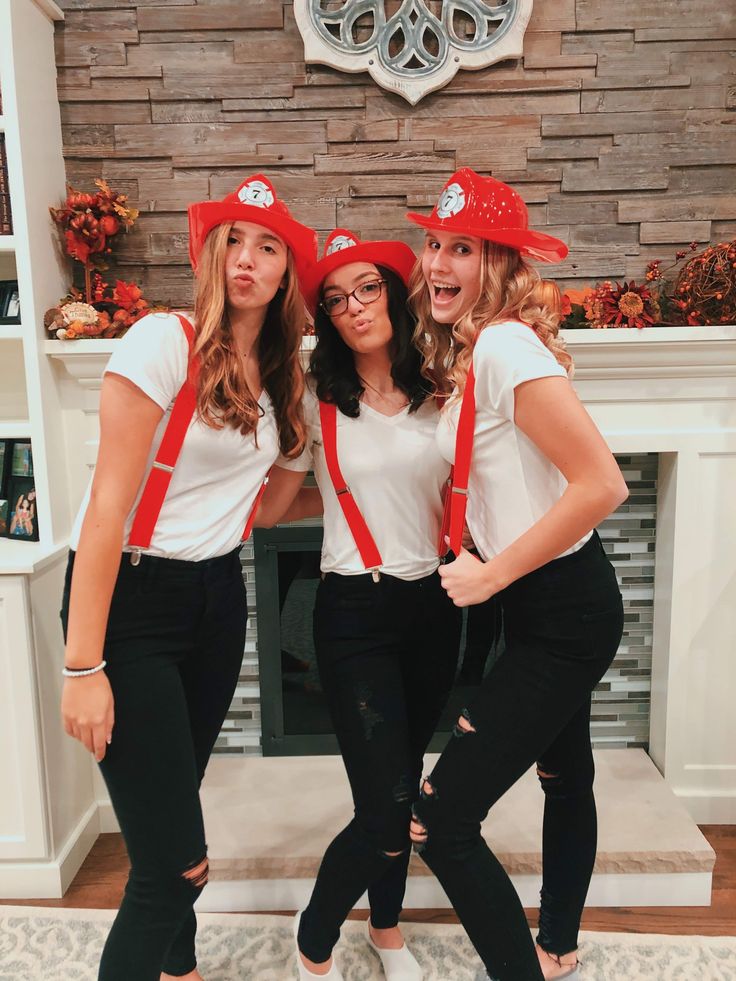 three women wearing red hats and suspenders posing for a photo in front of a fireplace