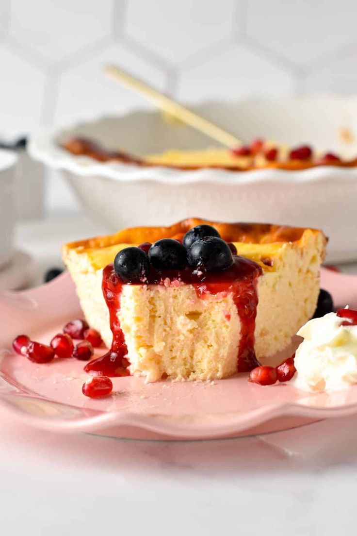 a piece of cake on a pink plate with blueberries and whipped cream in the background