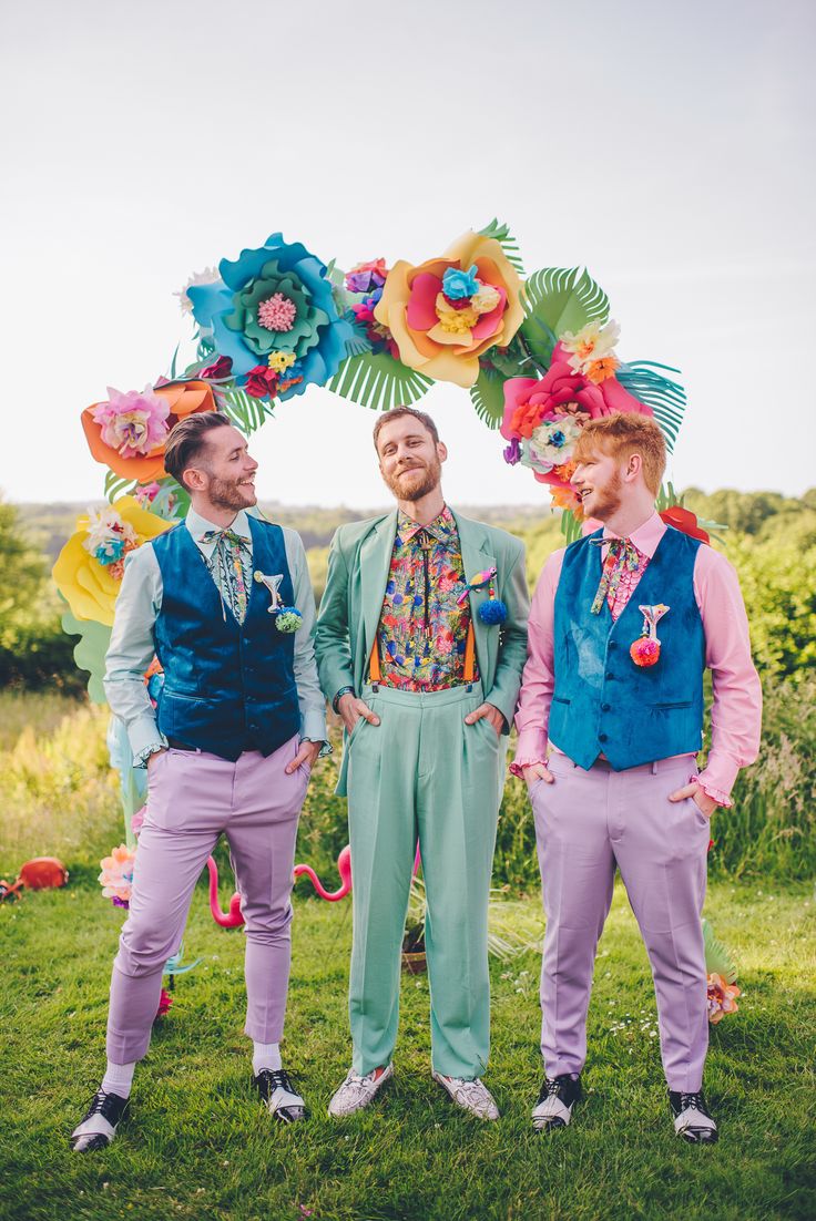 three men standing next to each other in front of an arch with flowers on it