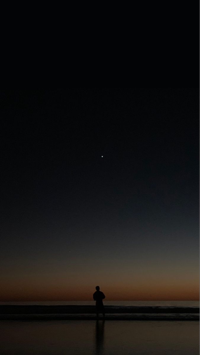 a man is standing on the beach at night with his back to the camera and looking into the distance