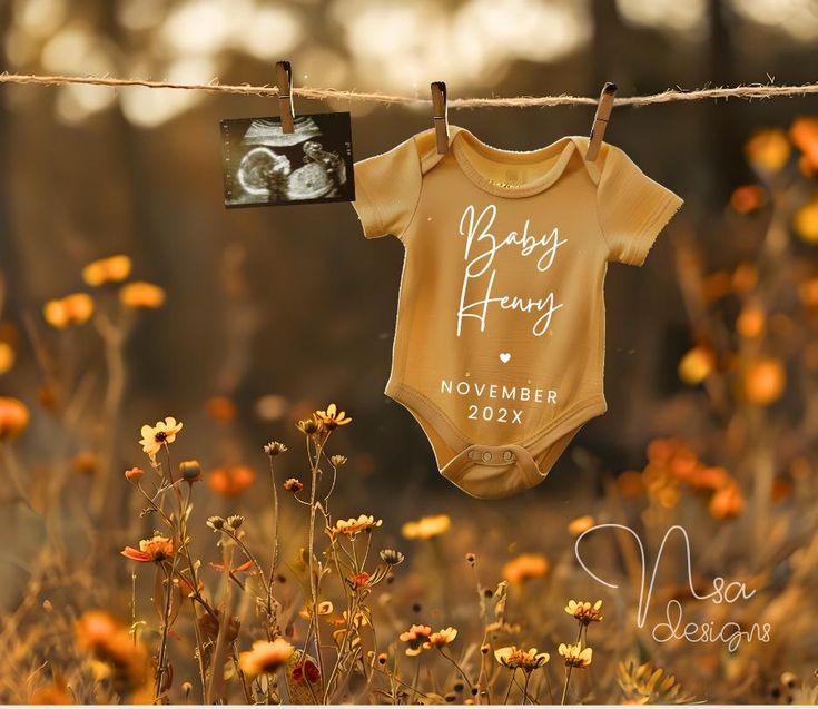 a baby's bodysuit hanging on a clothes line with flowers in the background