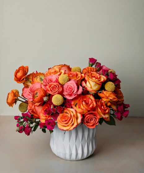 a white vase filled with lots of orange and pink flowers on top of a table