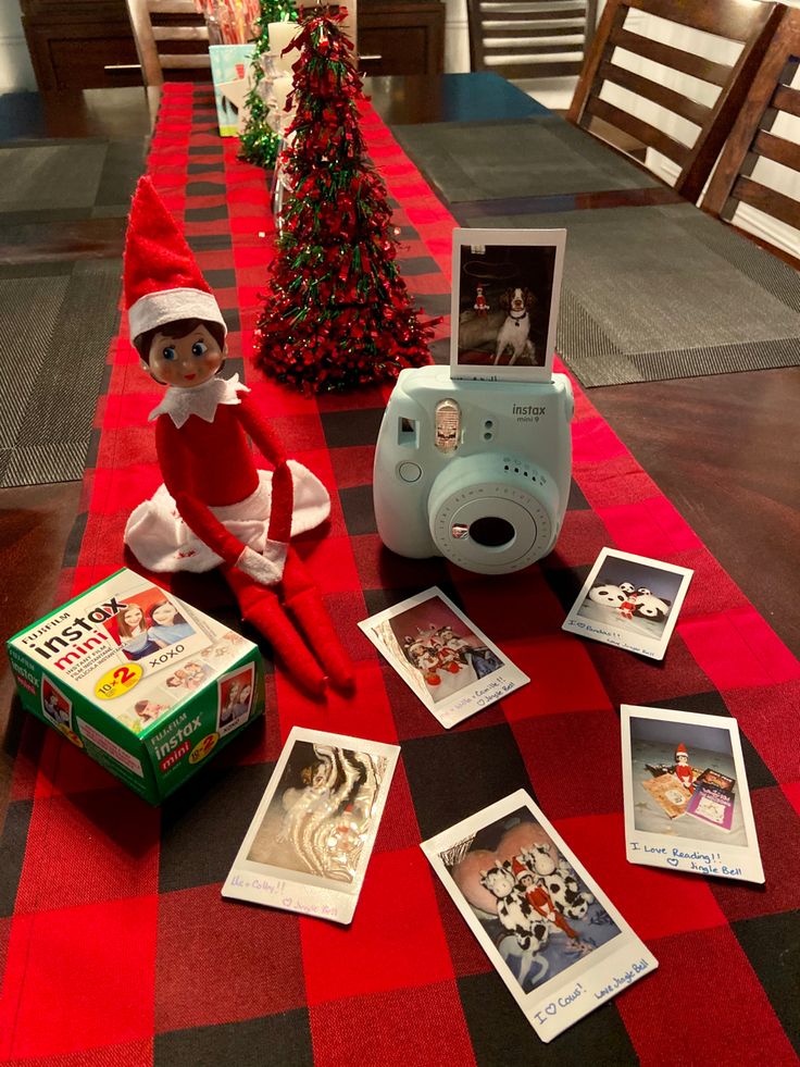 an elf is sitting on the floor next to some christmas cards and a digital camera