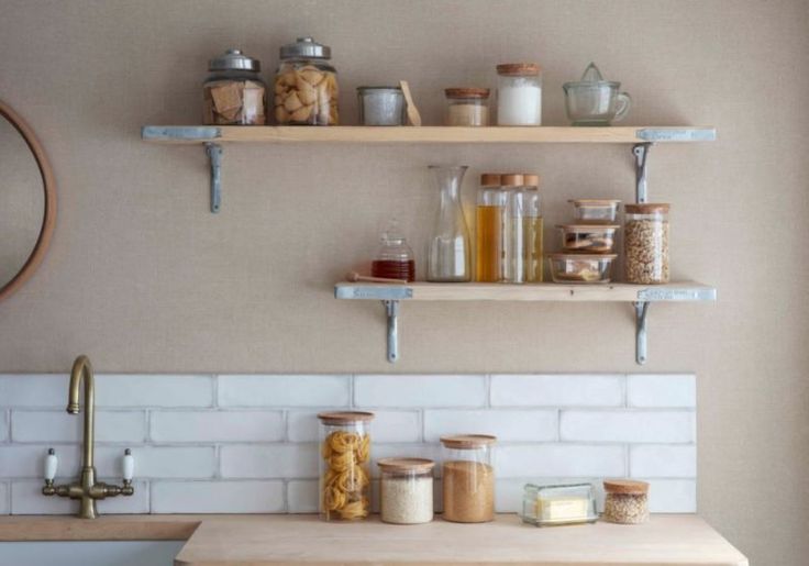 two shelves above a kitchen sink filled with jars and other items on top of it