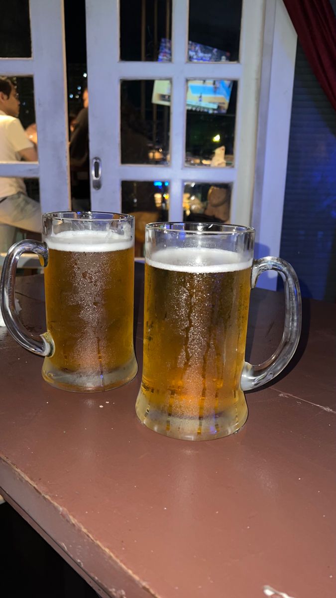 two mugs of beer sitting on top of a table