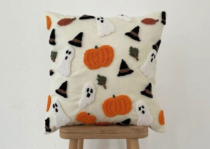 a white pillow with pumpkins and ghost faces on it, sitting on a wooden stool