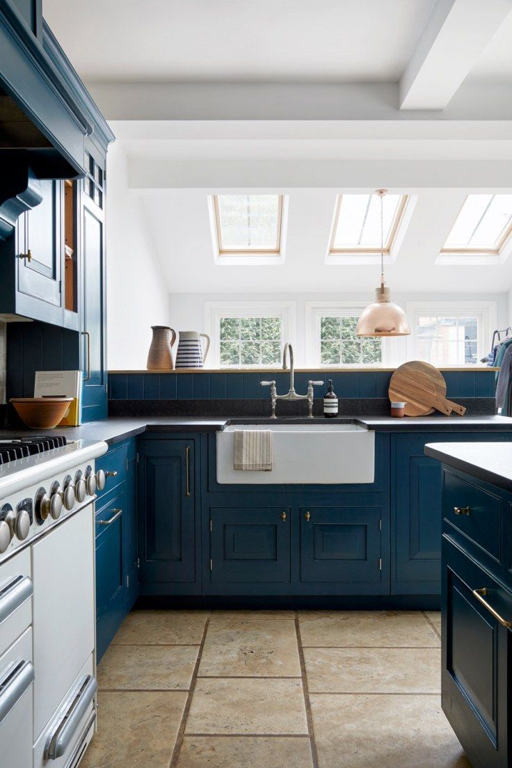 a kitchen with blue cabinets and tile flooring, white walls and skylights above the sink