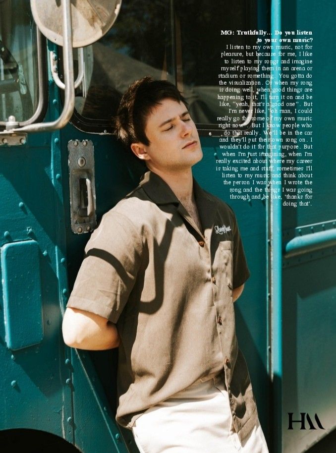 a young man leaning against the side of a green truck with his hands on his hips