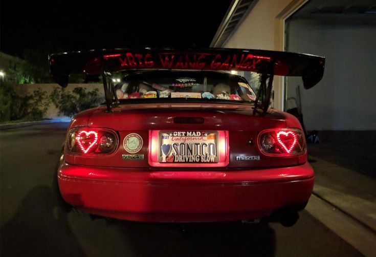 the back end of a red sports car with its hood up and lights on at night