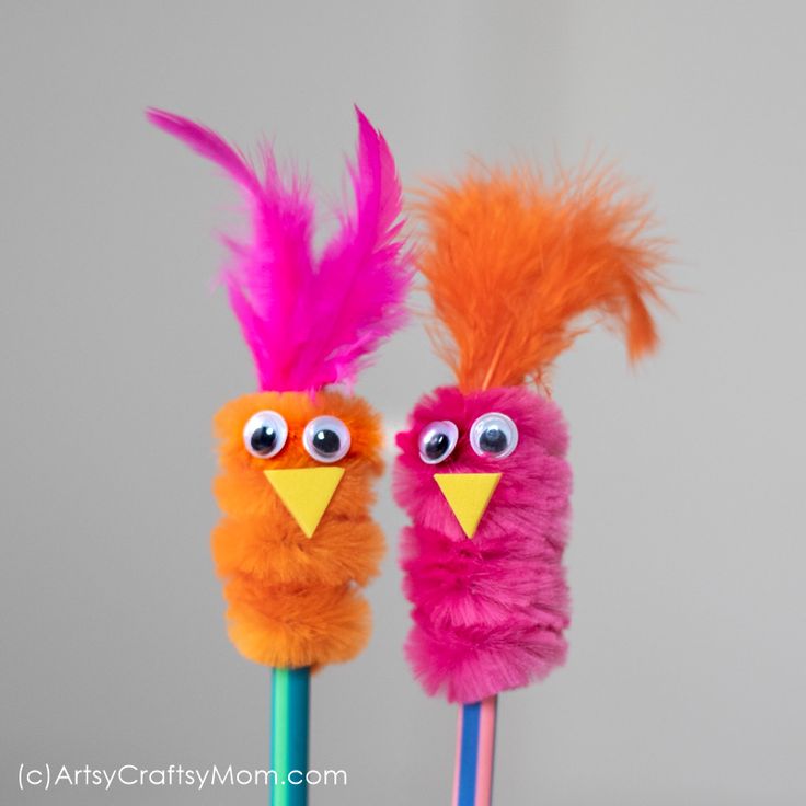 two colorful feathers on top of toothbrushes with googly eyes and beaks