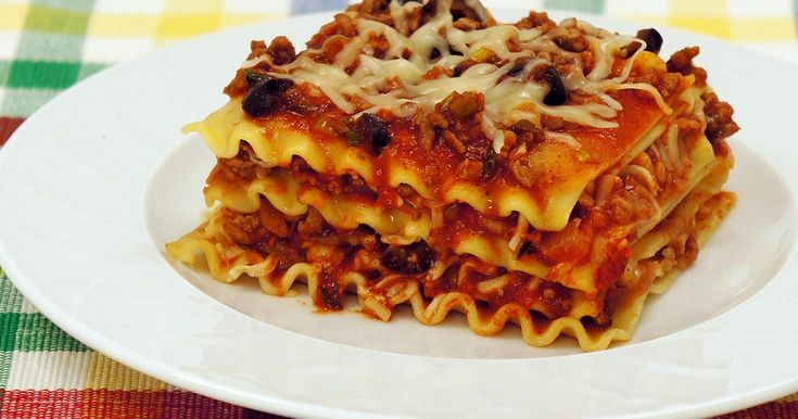 a white plate topped with lasagna casserole covered in sauce and cheese