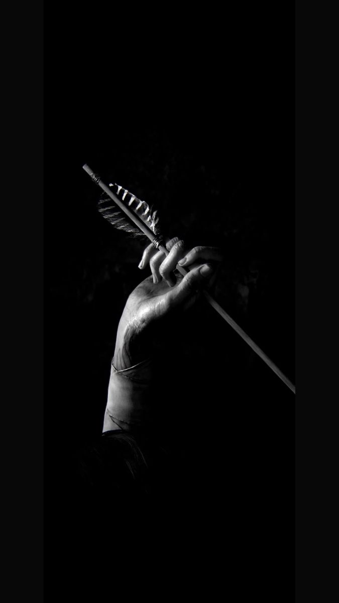 black and white photograph of a person holding an arrow in the dark with their hand