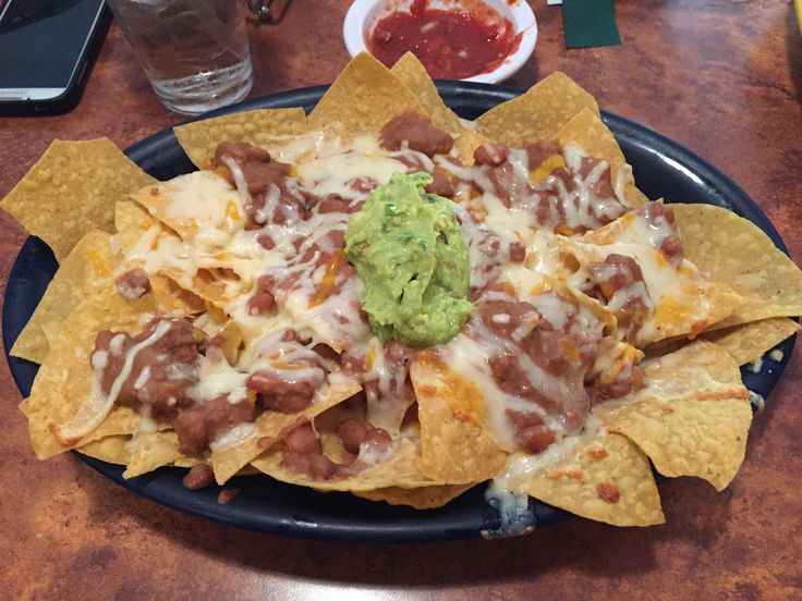 nachos with guacamole and salsa are on a black platter