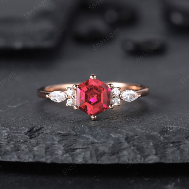 an engagement ring with a red stone surrounded by three diamonds on top of a rock