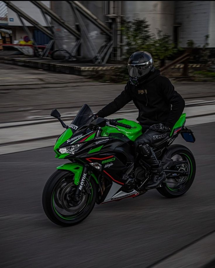 a person riding a green and black motorcycle on a street with buildings in the background