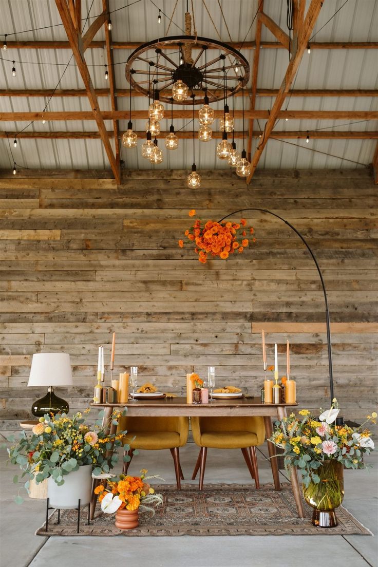 a dining room table with flowers and candles on the table in front of an old wooden wall