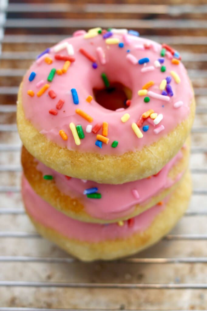 three donuts with pink frosting and sprinkles on a cooling rack