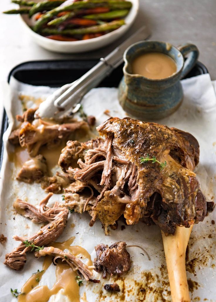 a tray filled with meat and sauce next to a plate of asparagus on a table