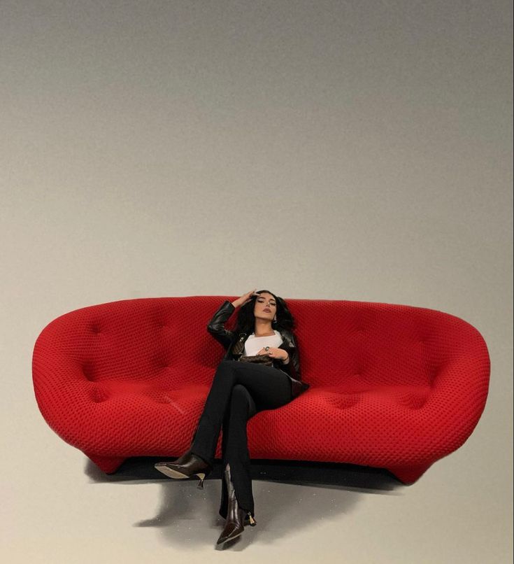 a woman sitting on top of a red couch with her eyes closed and hands behind her head